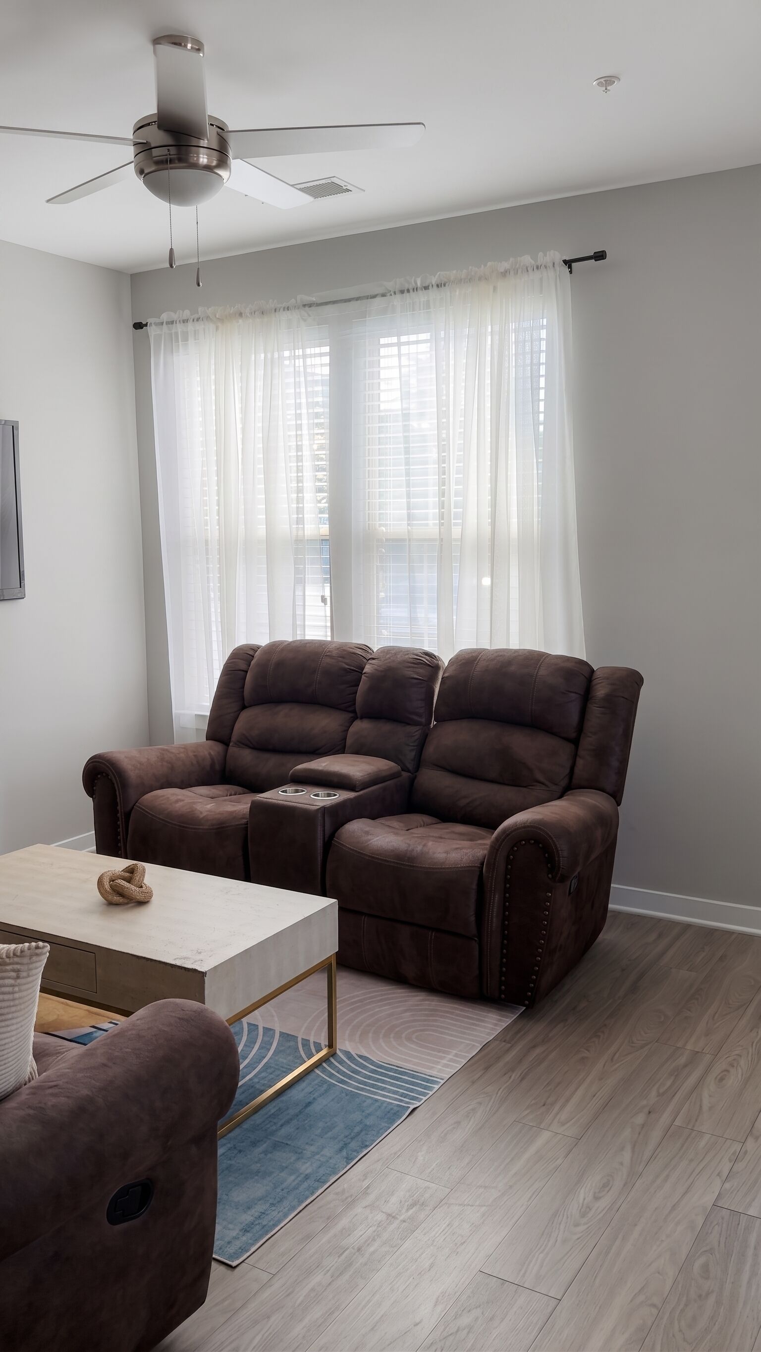 Een moderne woonkamer met een bruine leren bank, een witte salontafel en een plafondventilator.