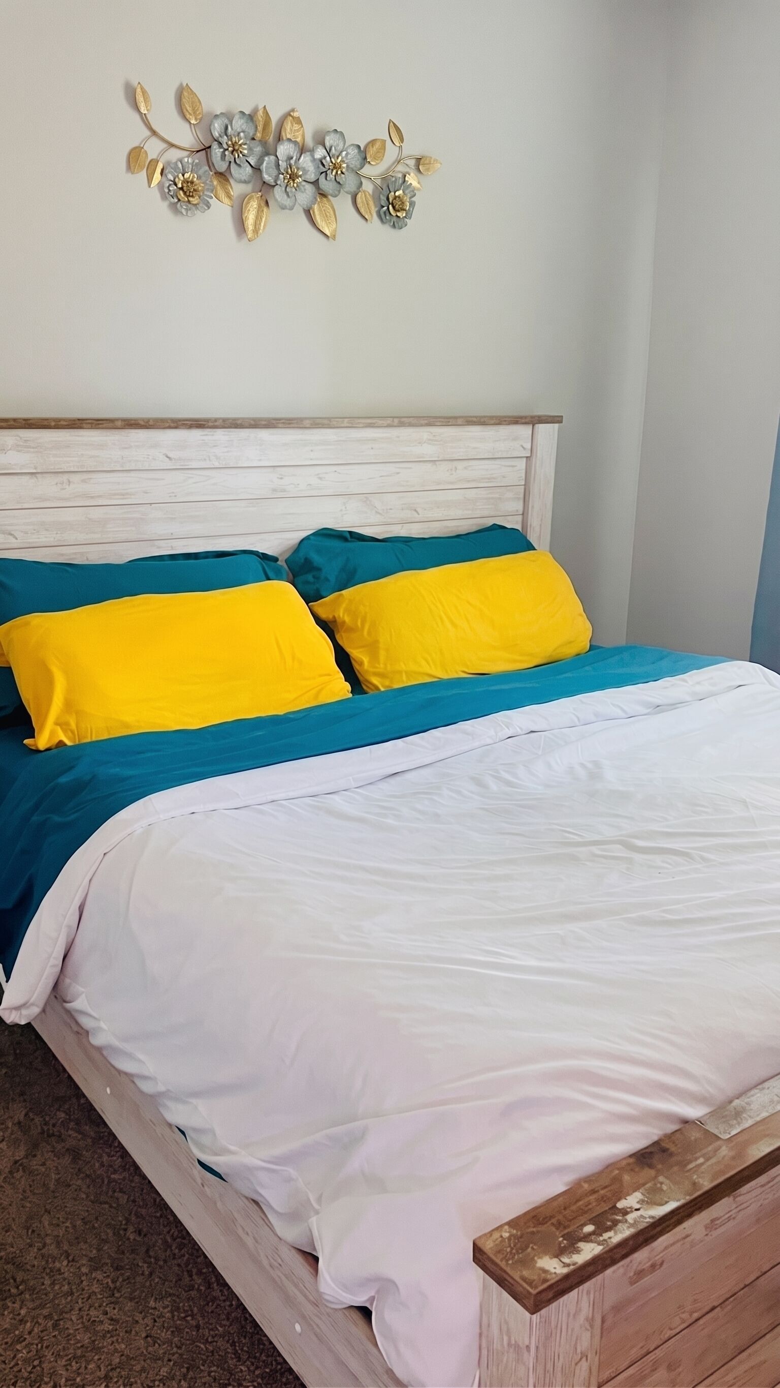 Een bed met witte lakens, blauwe en gele kussens en een houten hoofdbord.