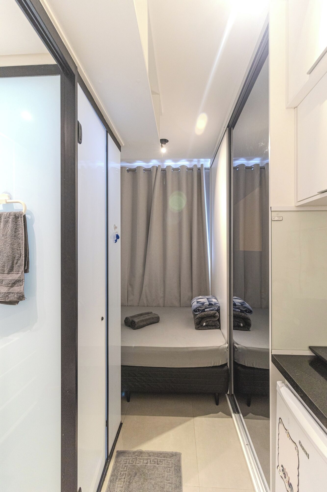 Habitación pequeña con cama, una mesita, un espejo y una puerta que da a otra estancia.