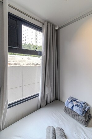 A small, single-bed room with a window, a view of a building outside, and a folded blanket on the bed. - VN Higienópolis, 450 meters from the Santa Cecília Metro Station (São Paulo)