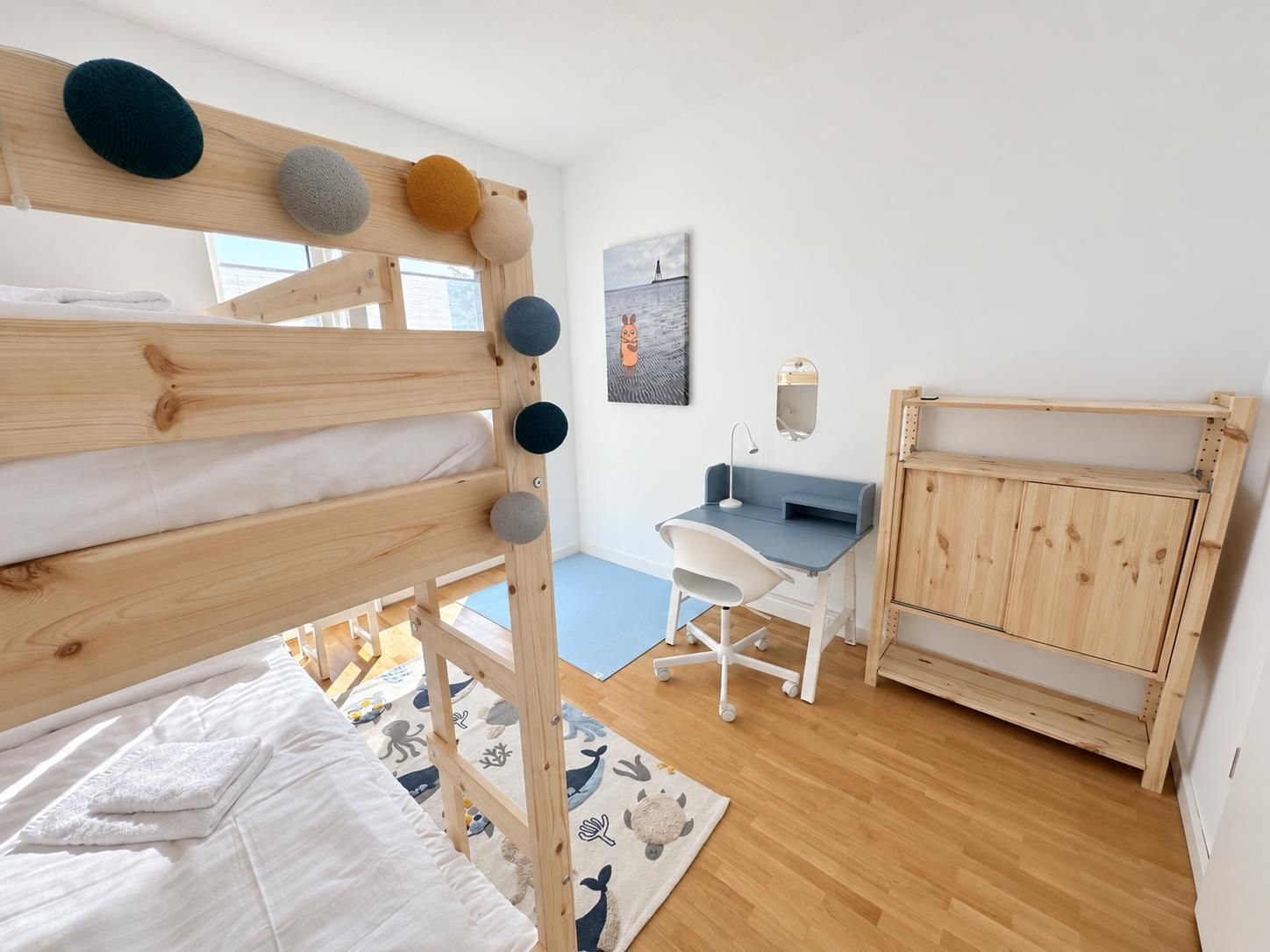 A child's bedroom with a bunk bed, desk, chair, and a cabinet.