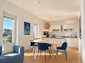 Eine moderne Küche mit weißen Schränken, einem Esstisch mit blauen Stühlen und einer Pendelleuchte.