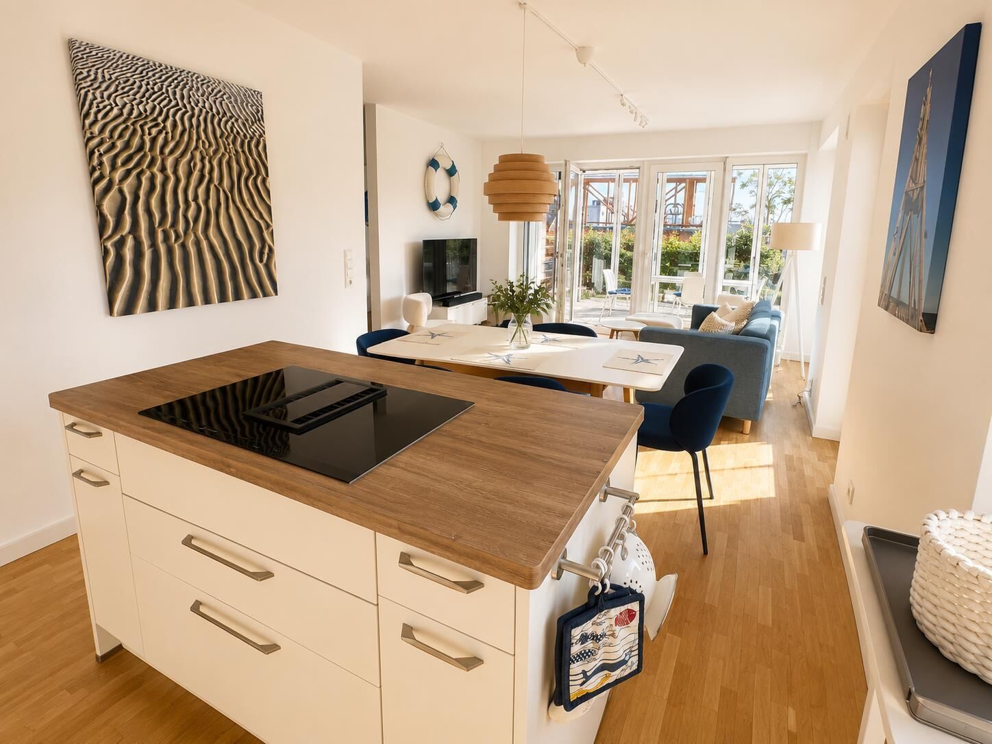 A modern kitchen with a built-in stove, white cabinetry, and a dining area with a blue chair and a table.