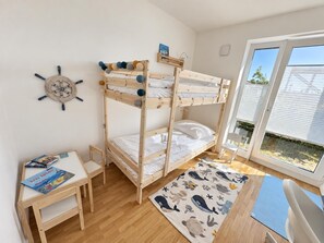 Ein Schlafraum mit Etagenbetten, einer Holzwanddekoration, einem kleinen Tisch mit Büchern und Blick durch eine Glastür.