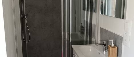 Un bagno moderno con cabina doccia in vetro, un lavandino bianco e uno specchio sopra.