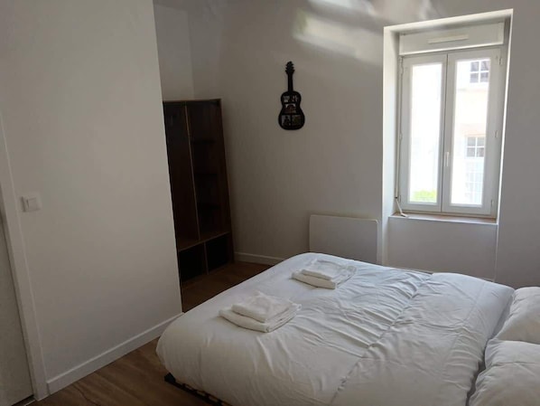 A bedroom with a bed, a window, and a guitar on the wall.