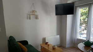 Una sala de estar con un sofá, una mesa de centro de madera, un televisor de pantalla plana y una ventana con cortinas.