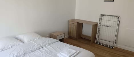 A hotel room with a bed, a desk, a nightstand, and a radiator.