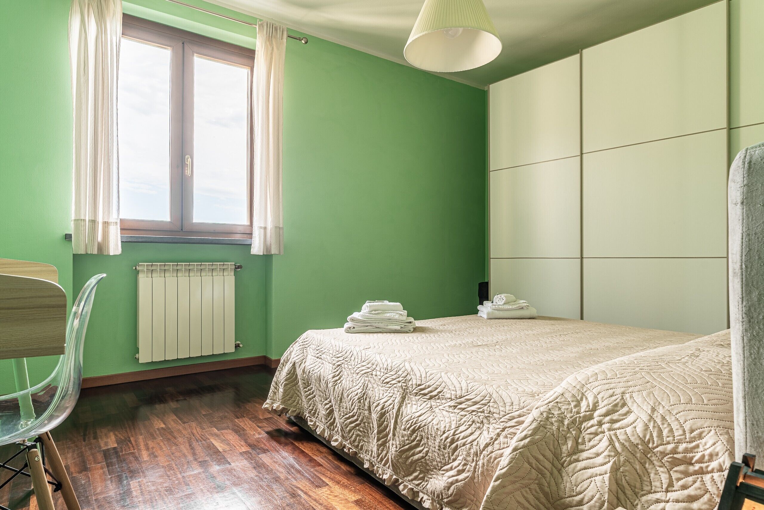 Een kamer met een bed, een stoel, een radiator en een raam met gordijnen.