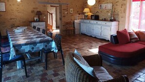 A dining area with a long table, chairs, and a red sofa. - Gite proche Puy duFou (La Boissière-de-Montaigu)