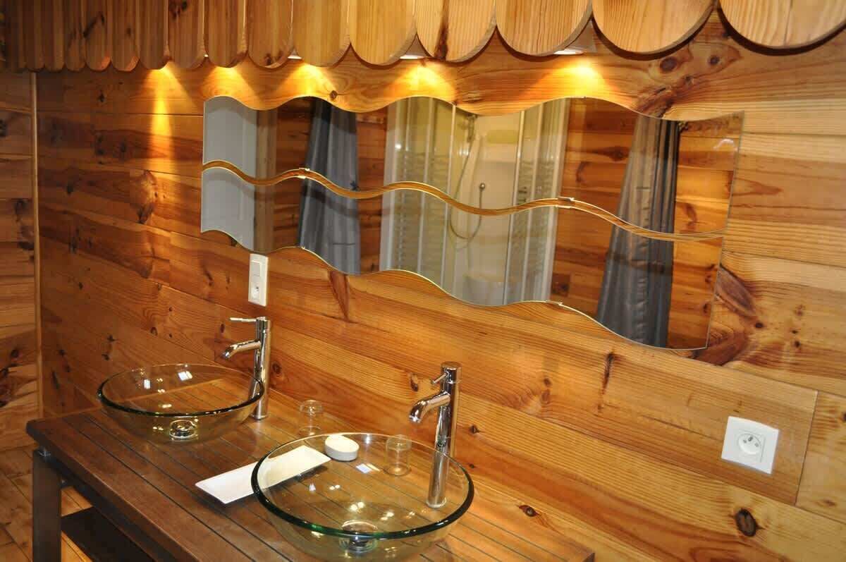 A wooden bathroom with two glass sinks and a large mirror.