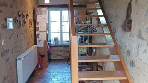 A narrow staircase with wooden steps leading to a landing, a radiator on the left, and a window with natural light. - Gite proche Puy duFou (La Boissière-de-Montaigu)