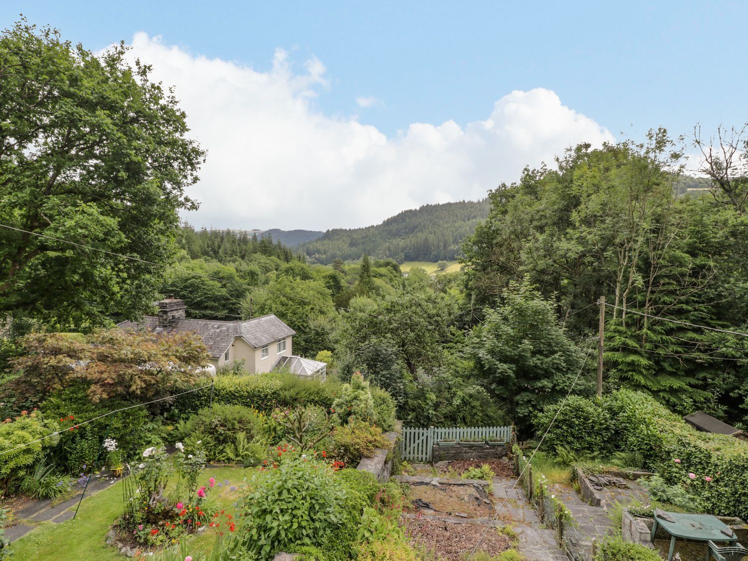 Ländliche Landschaft mit einem Haus, umgeben von üppiger Vegetation und Hügeln im Hintergrund.