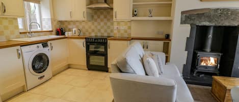 A compact kitchen with a washing machine, oven, and a built-in wood stove.