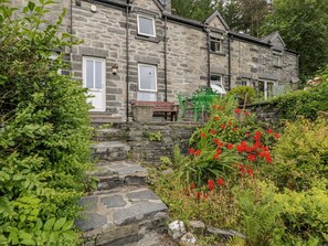 A stone building with a stone staircase leading to a door, surrounded by lush greenery and red flowers. - Awelfryn (Betws-Y-Coed)