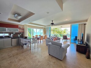 A modern living space with a kitchen, dining area, and seating with a view of the ocean. - 304 Ocean One Condos Luxury Beachfront Vacation Rental in Barbados (Maxwell)