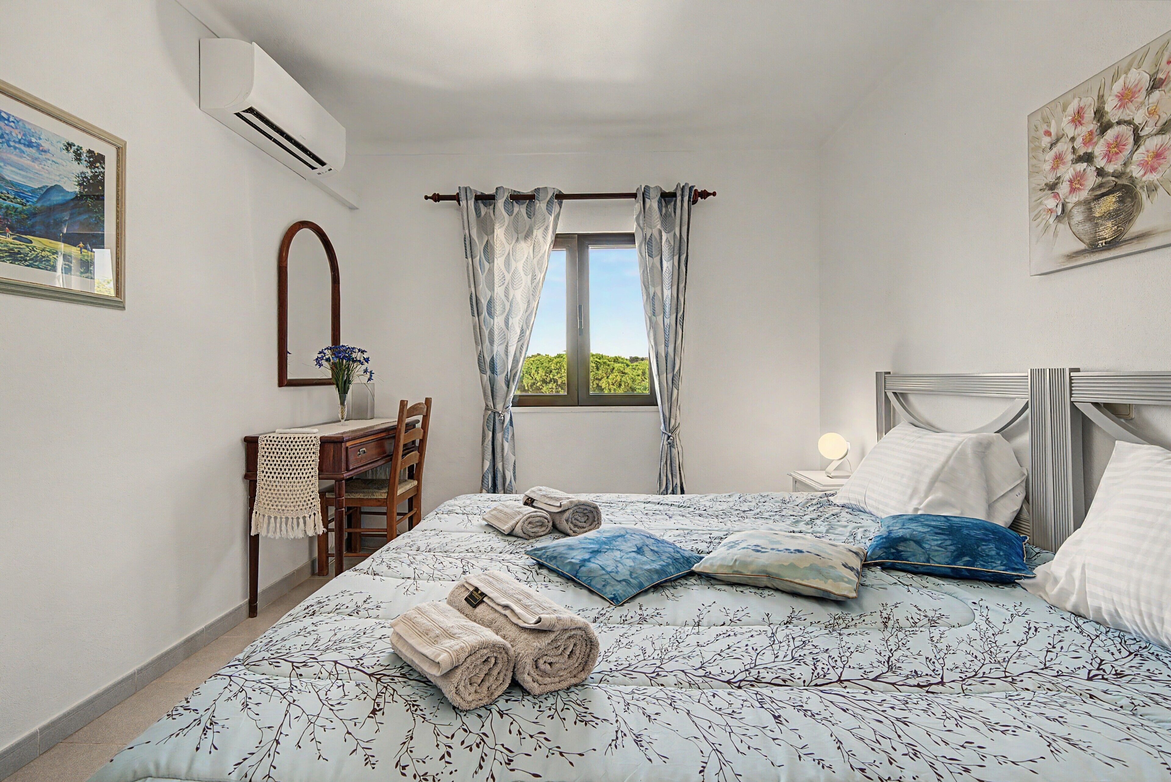 A bedroom with a bed, a desk, a chair, a mirror, and a window with curtains.