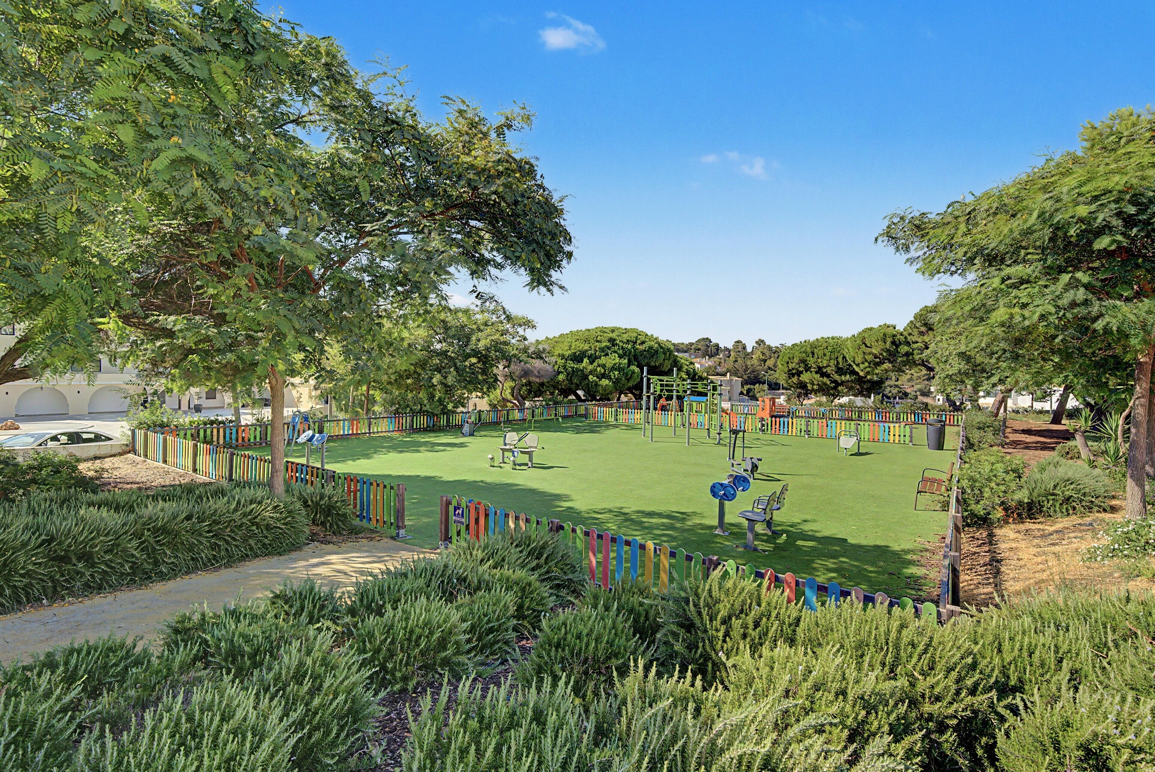 Un parque con césped verde, juegos infantiles y una valla colorida.
