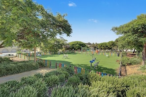 A park with a green lawn, playground equipment, and a colorful fence. - Apartment 'T1 na Praia de Centeanes' in Front of the Beach, Carvoeiro (Carvoeiro)