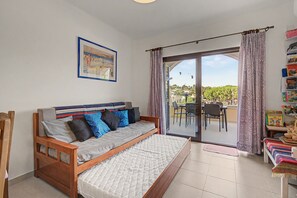 A room with a wooden bed, a sofa, a dining area with chairs and a table, and a view of the outdoors. - Apartment 'Apartamento Praia Carvoeiro' with Balcony, Wi-Fi and Air Conditioning (Carvoeiro)