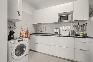 A modern kitchen with white cabinets, a built-in microwave, a coffee machine, and a washing machine. - Apartment 'T1 na Praia de Centeanes' in Front of the Beach, Carvoeiro (Carvoeiro)