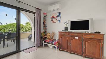 Un salón con puerta corrediza de vidrio que da a un balcón, un televisor, una estantería y un mueble de madera.