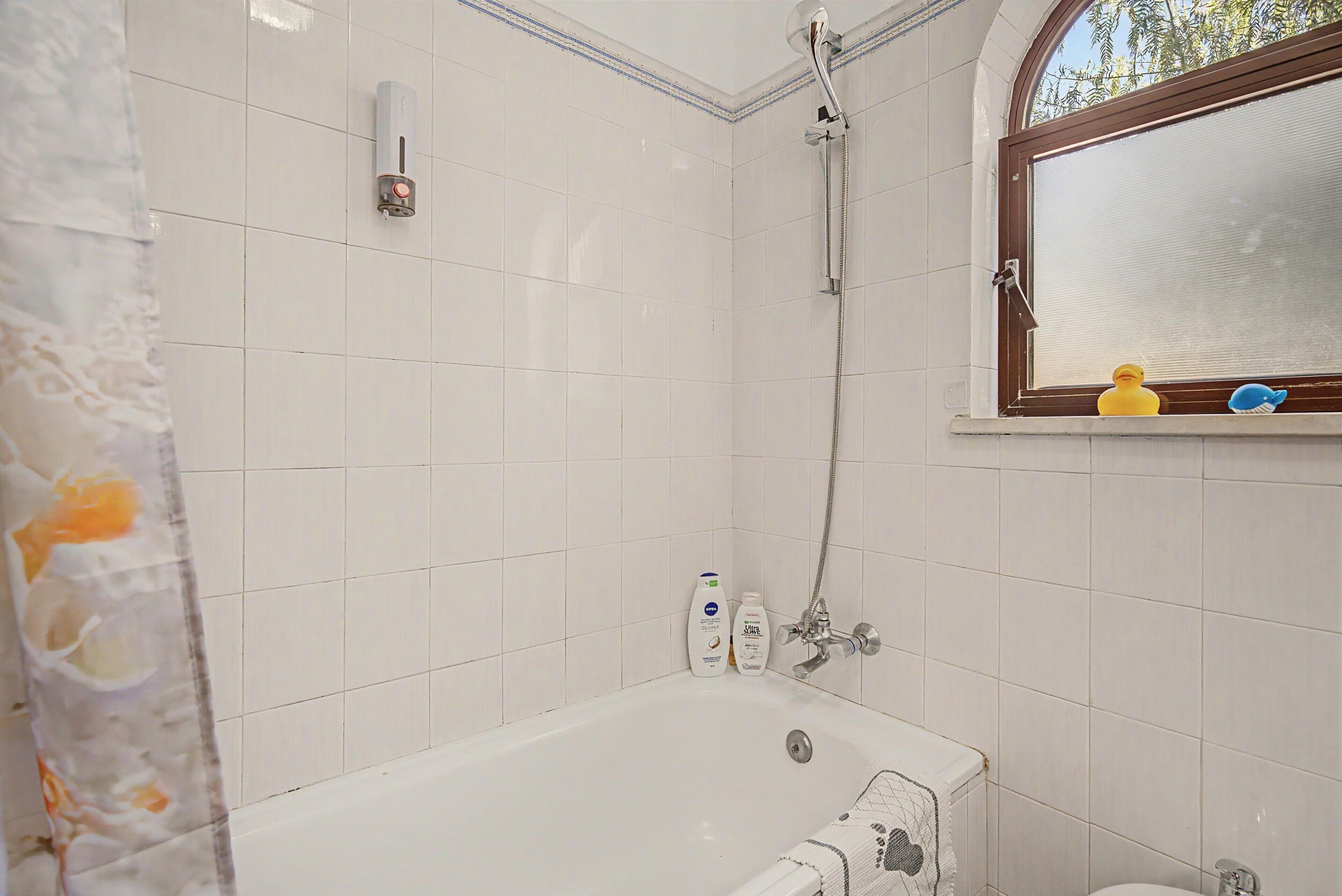 Un baño con bañera, ducha y ventana con juguetes en el alféizar.