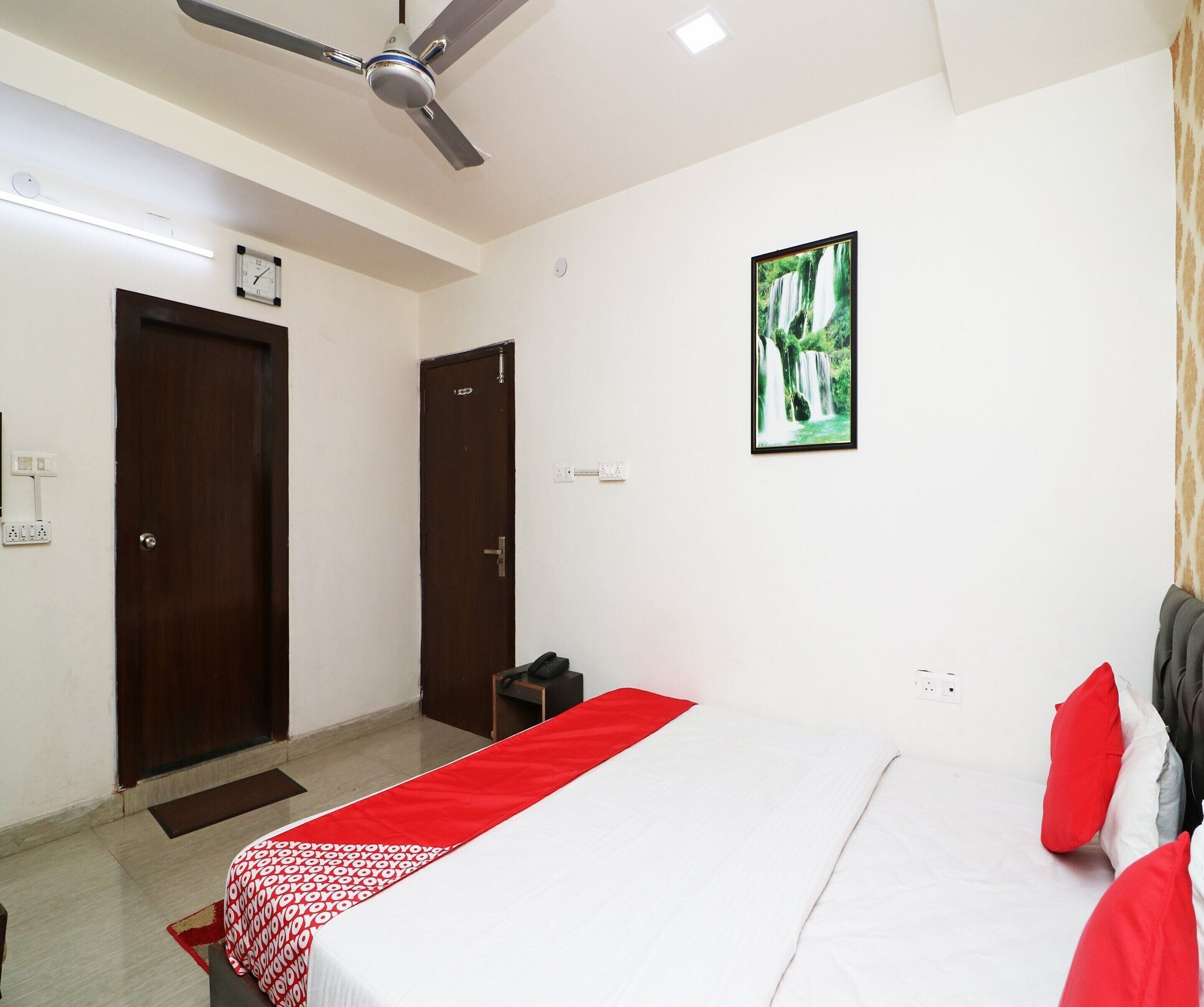 A hotel room with a bed, a ceiling fan, a clock, and a framed picture on the wall.
