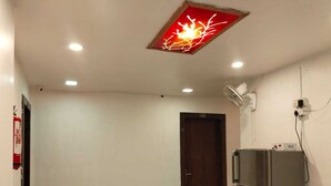 Una habitación con puerta, refrigerador, ventilador de pared y lámpara en el techo.