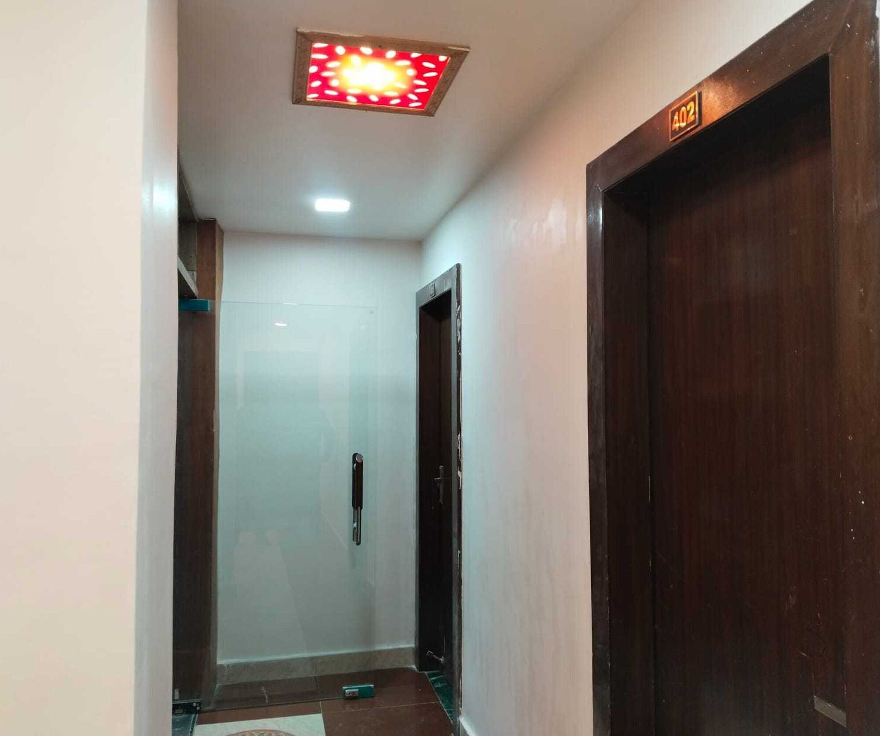 A hallway with a wooden door, a white wall, and a ceiling light fixture.