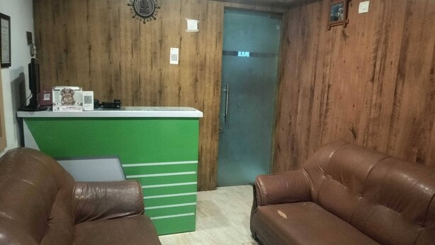 Un área de recepción con pared de madera, mostrador verde y dos sofás de cuero.