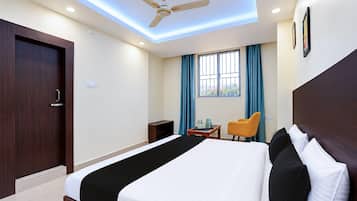 Habitación de hotel con cama, escritorio, silla, ventilador de techo y ventana con cortinas.