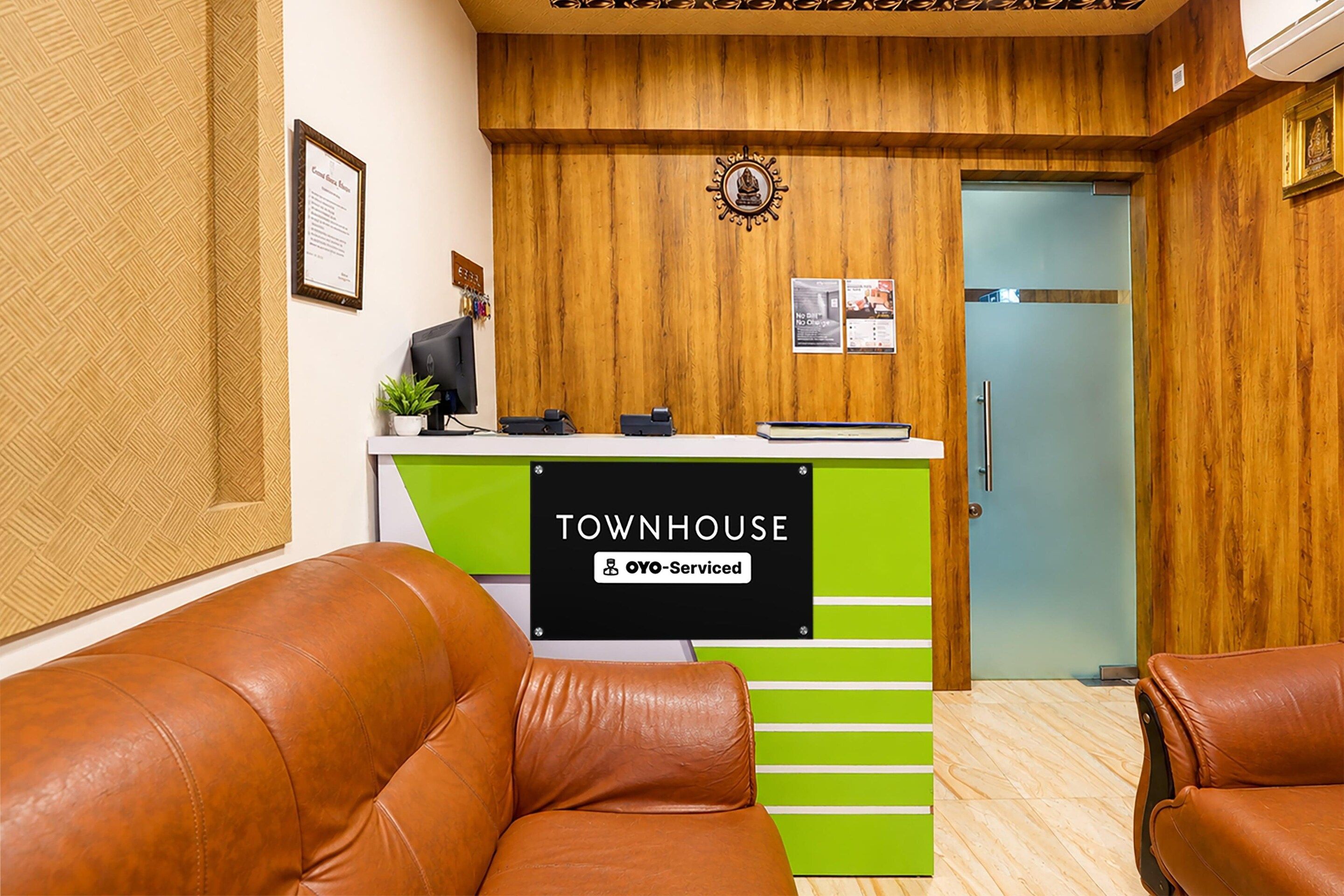 A reception area with a wooden wall, a reception desk labeled 'TOWNHOUSE' and 'Oyo-Serviced', a door, and leather seating.