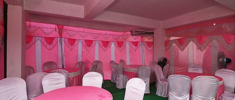 A banquet hall with round tables covered in pink tablecloths, white chairs with silver sashes, and pink draped curtains.