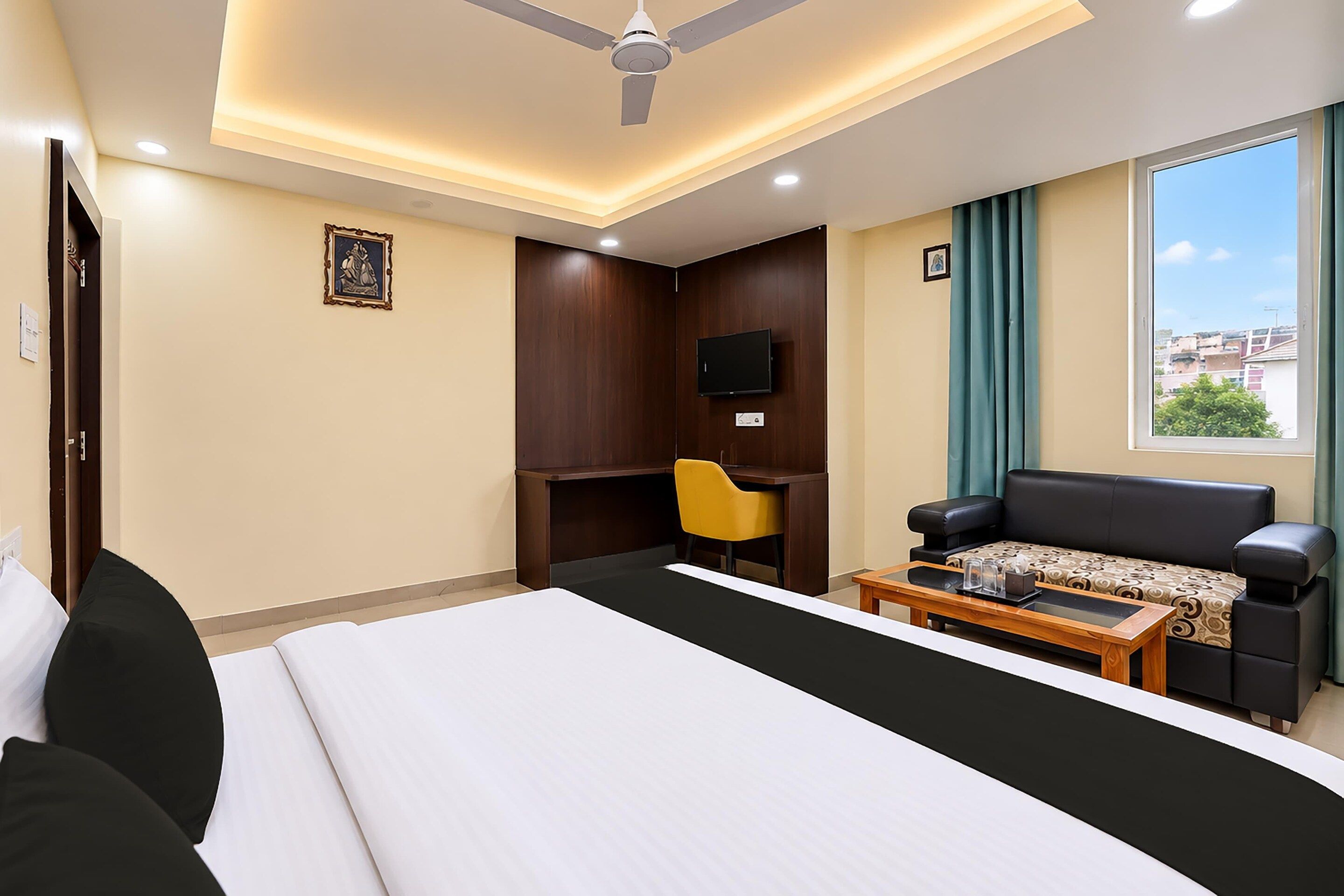 A hotel room with a bed, a desk, a chair, a sofa, a coffee table, a TV, and a window with a view.