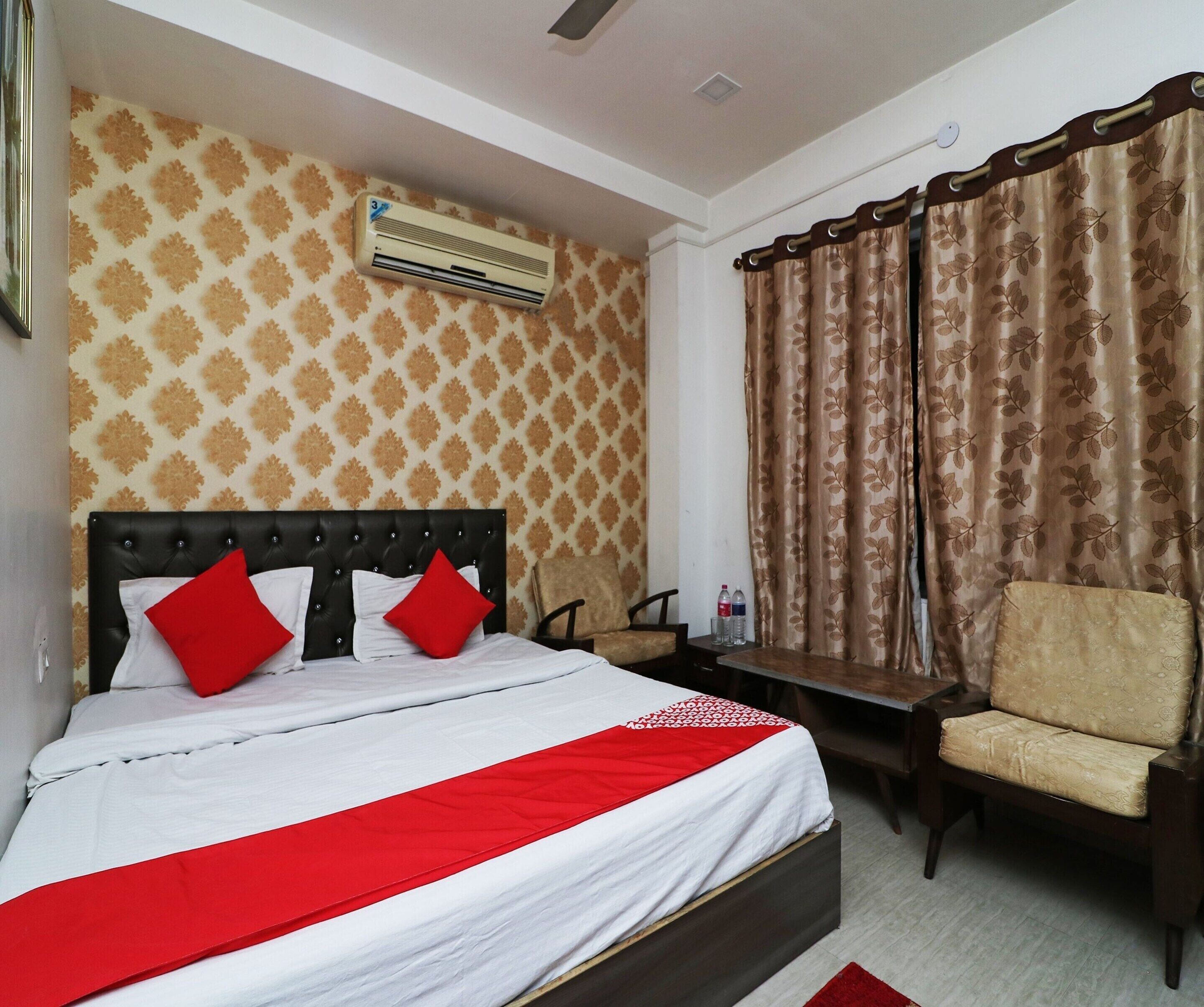 A hotel room with a bed, a chair, a table, an air conditioning unit, and curtains.