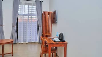 A room with a wooden table, two chairs, a TV mounted on the wall, and a window with curtains.