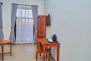 Una habitación con una mesa de madera, dos sillas, un televisor montado en la pared y una ventana con cortinas.