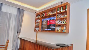 A bar area with wooden shelves stocked with bottles, a reception desk, and a television screen.