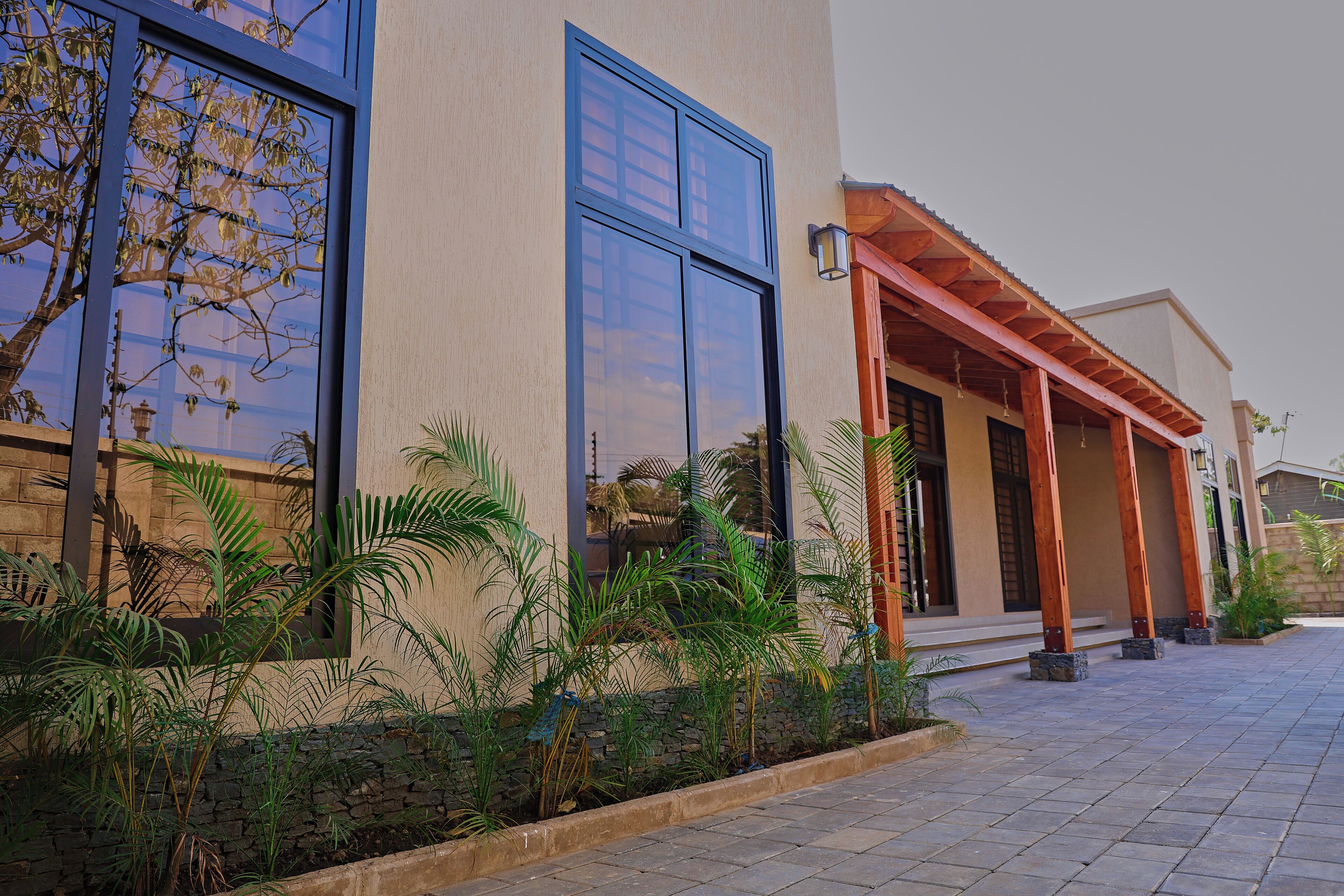 A modern building with large windows, a covered porch, and a stone wall with greenery.