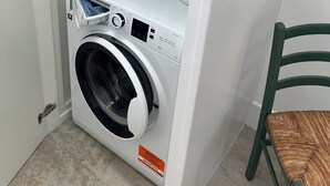 A compact washing machine with a control panel, two detergent bottles, and a chair. - Newly completed barn conversion in picturesque village of Sidbury. (PQ9H+949 Sidmouth)