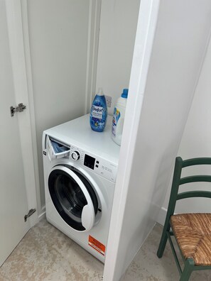 Eine kompakte Waschmaschine mit Bedienfeld, zwei Waschmittelbehältern und einem Stuhl.