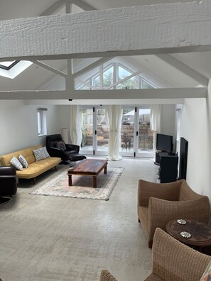 Ein geräumiges Wohnzimmer mit hoher Decke, einem Sofa, einem Couchtisch und einem Fernseher.
