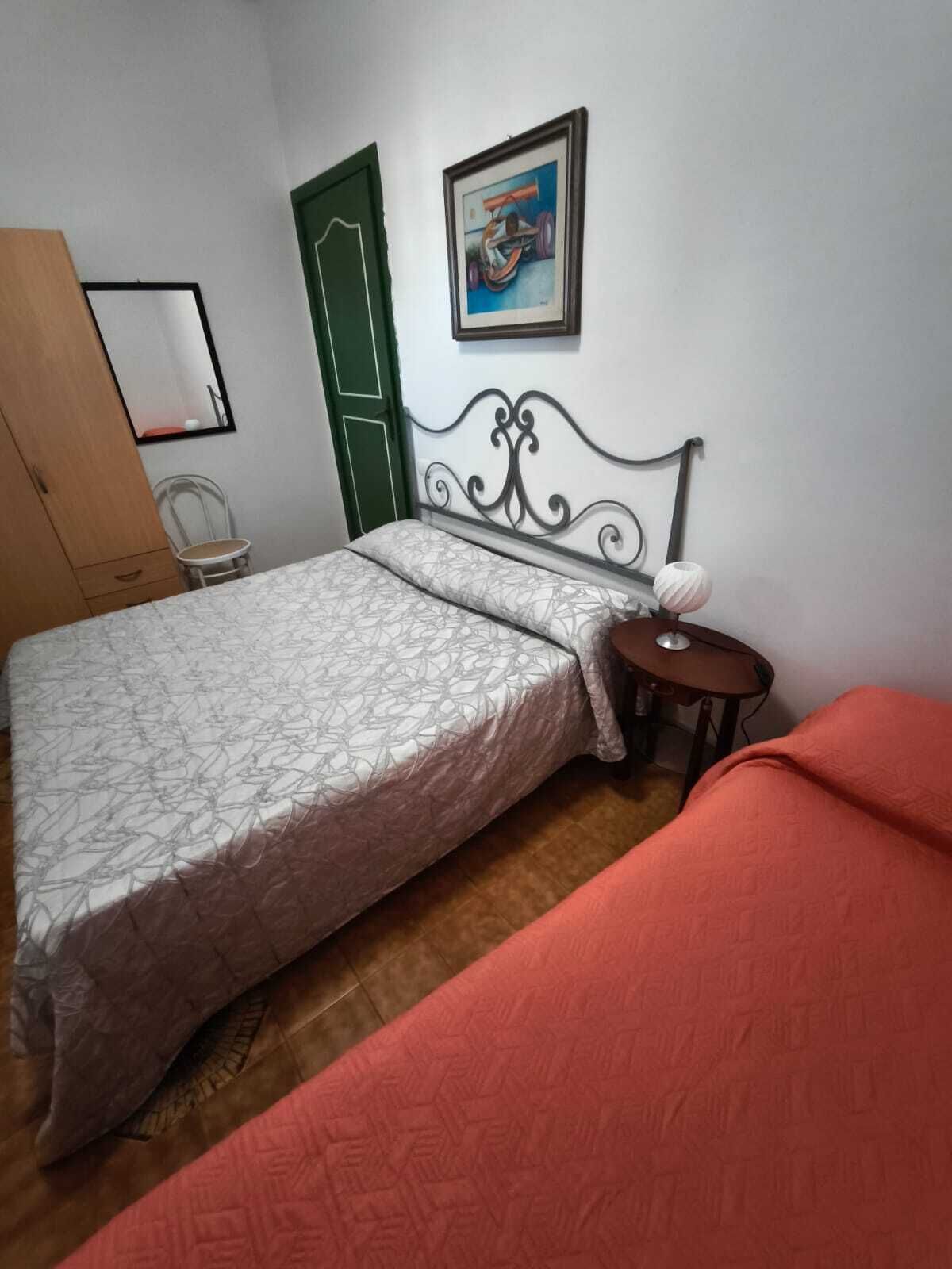 Une pièce avec un lit, une chaise, une petite table, une porte verte et un tableau accroché au mur.