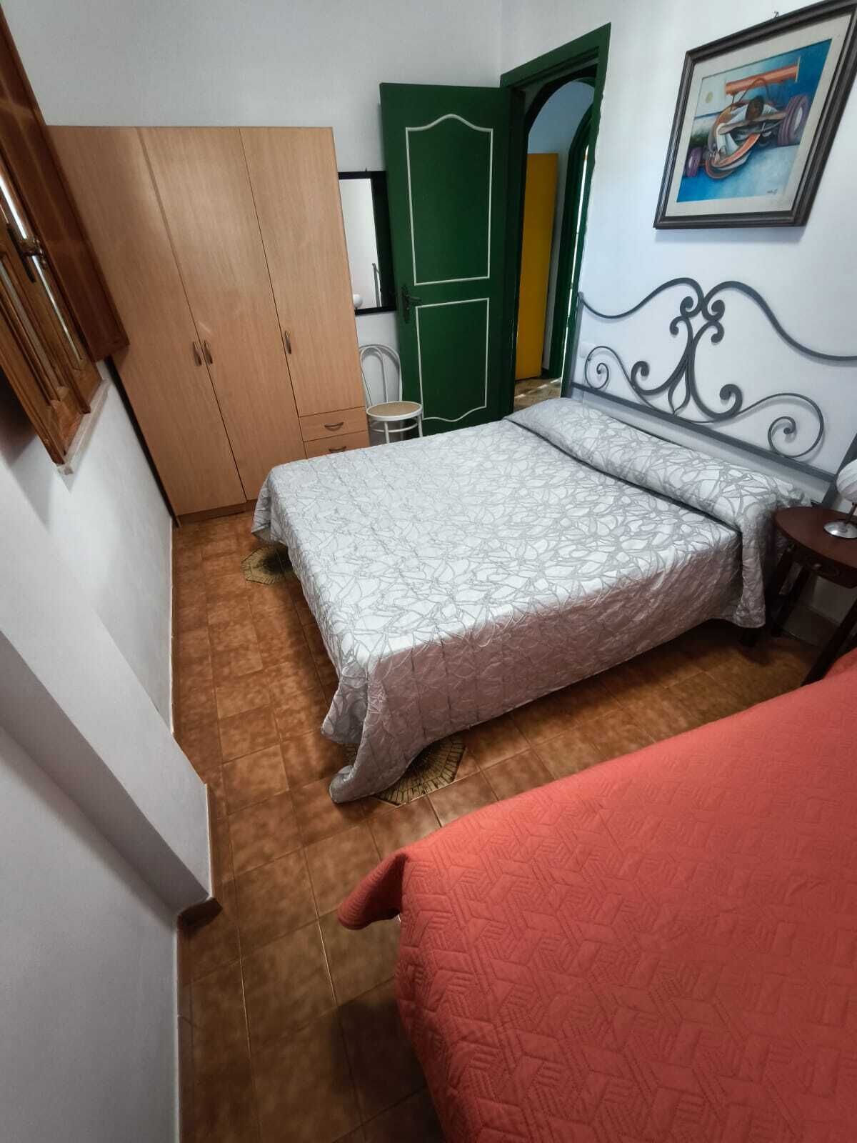 A bedroom with a bed, a green door, a small table, and a painting on the wall.