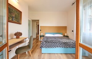 Quarto com cama, mesas de cabeceira, escrivaninha, cadeira e janela.