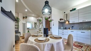 Zona pranzo moderna con tavolo rotondo imbandito per quattro persone, cucina con pensili bianchi e lampada a sospensione.