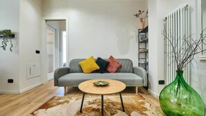 Un soggiorno con un divano grigio, un tavolino rotondo in legno, un vaso verde e un tappeto decorato.