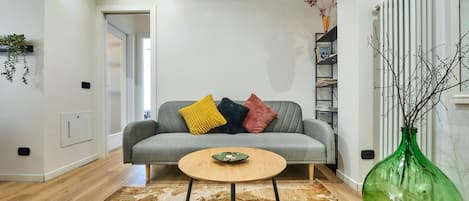 Un salon avec un canapé gris, une table basse ronde en bois, un vase vert et un tapis à motifs.