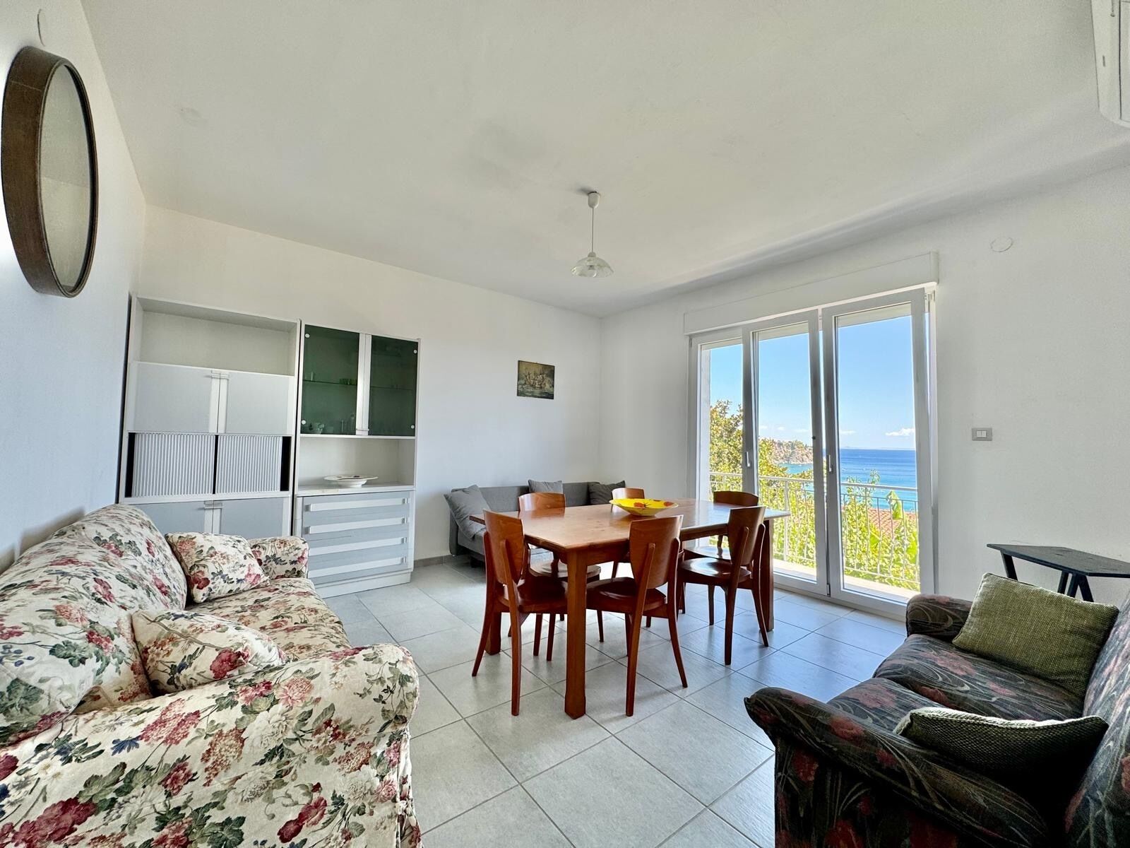 Ein Zimmer mit Esstisch, Stühlen, einer Couch und einem Balkon mit Blick.